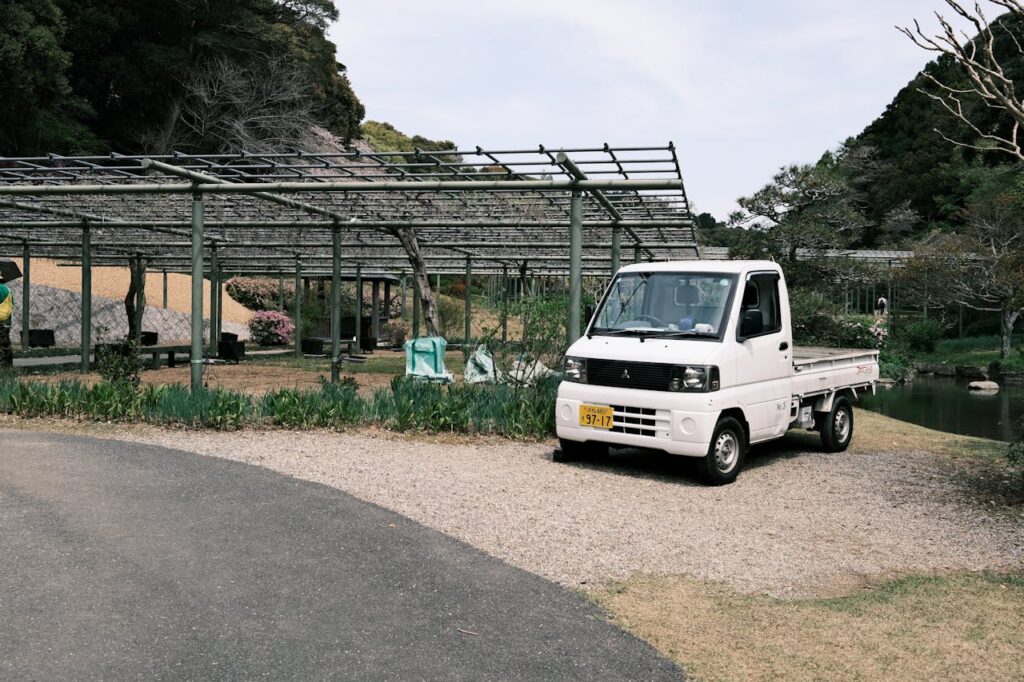 A small white truck parked near a pergola in a lush Japanese garden setting.
