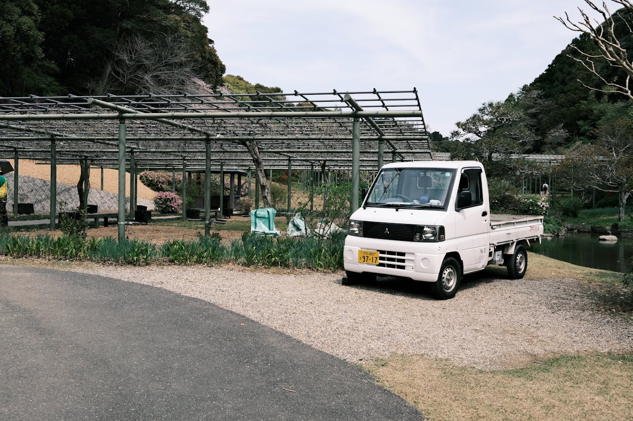 A small white truck parked near a pergola in a lush Japanese garden setting.