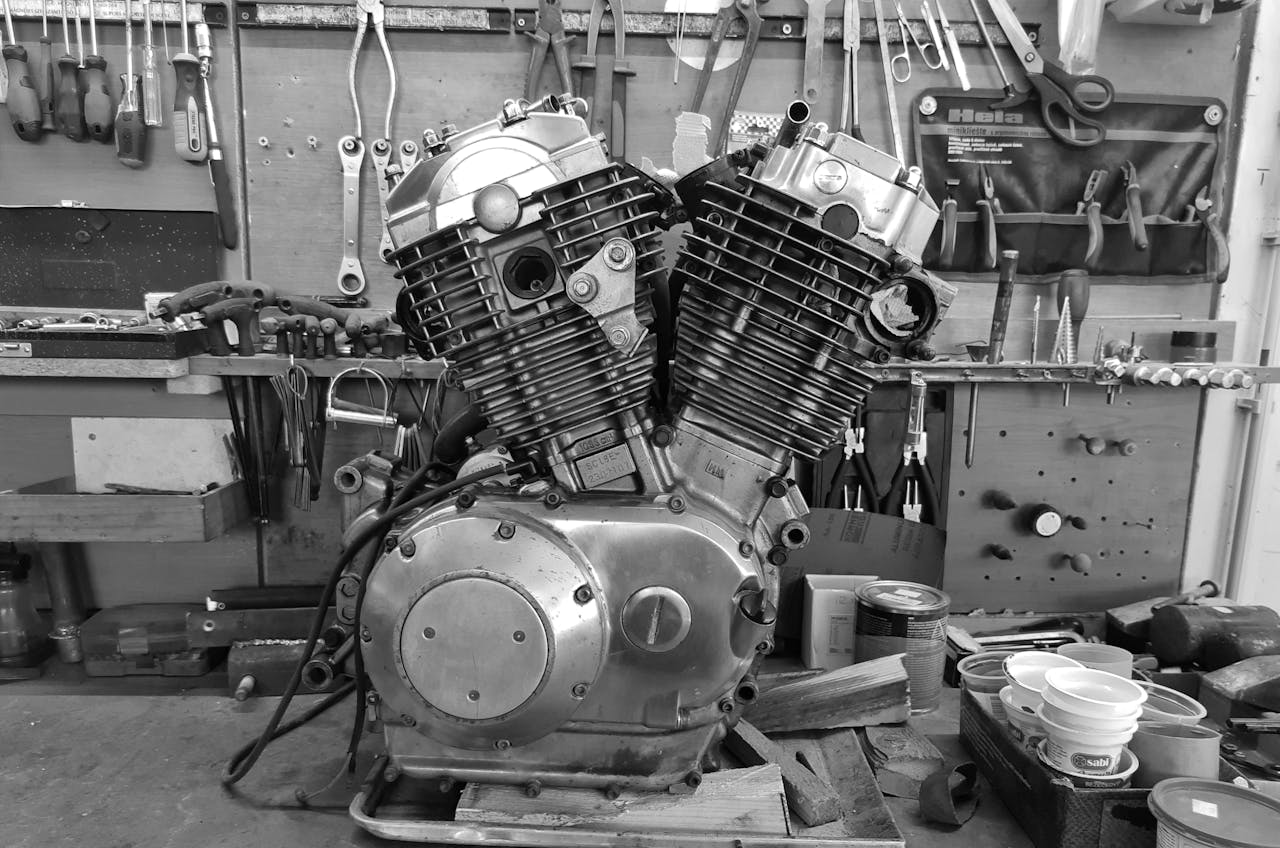 Black and white image of a vintage engine in a workshop with various tools hanging on the wall.
